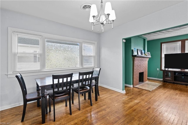 dining area featuring a fireplace, wood-type flooring, and a notable chandelier