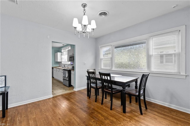 dining area with light wood-type flooring, an inviting chandelier, and sink