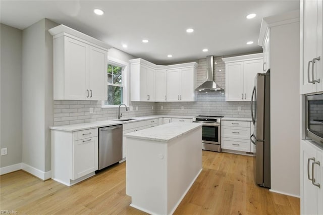 kitchen with wall chimney exhaust hood, a kitchen island, light wood-type flooring, and appliances with stainless steel finishes