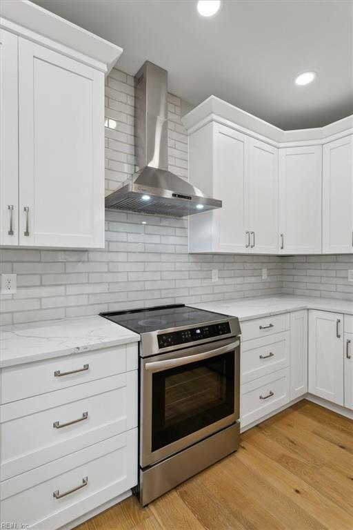 kitchen with decorative backsplash, wall chimney range hood, light hardwood / wood-style flooring, white cabinetry, and stainless steel range with electric cooktop