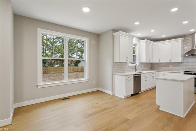 kitchen featuring white cabinetry, wall chimney range hood, appliances with stainless steel finishes, a kitchen island, and light wood-type flooring