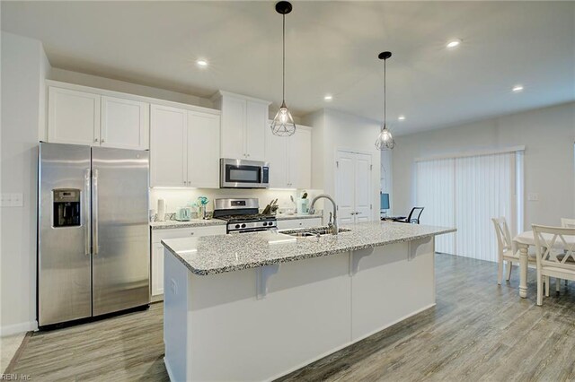 kitchen featuring sink, stainless steel appliances, an island with sink, white cabinets, and light wood-type flooring