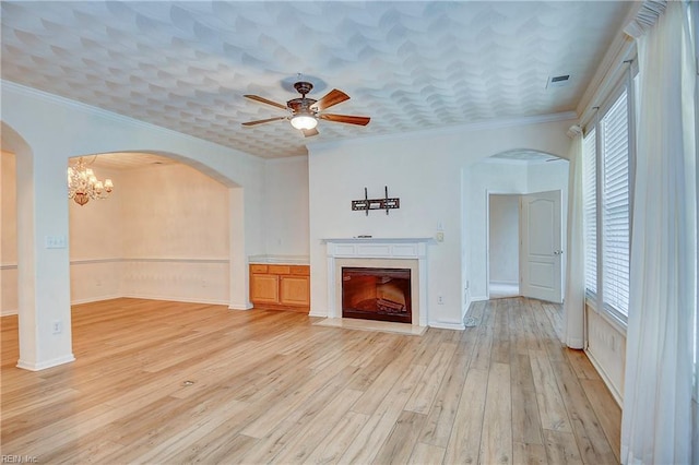 unfurnished living room with ceiling fan with notable chandelier, light hardwood / wood-style floors, ornamental molding, and a wealth of natural light