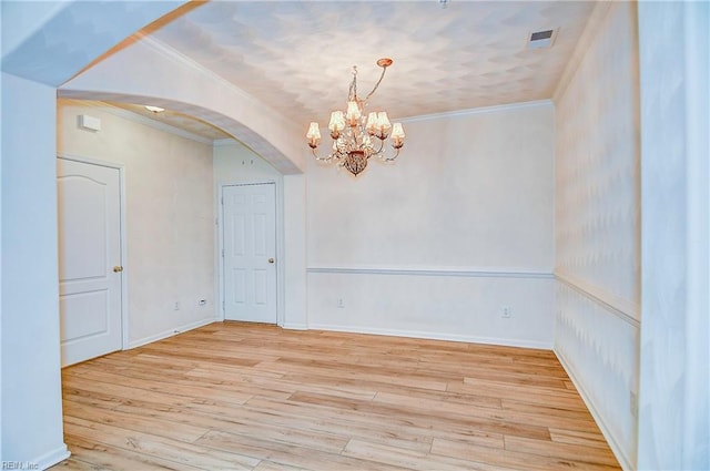 empty room featuring a chandelier, light wood-type flooring, and ornamental molding