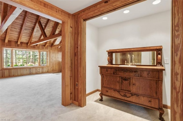 hall featuring vaulted ceiling with beams, wooden walls, sink, and light colored carpet