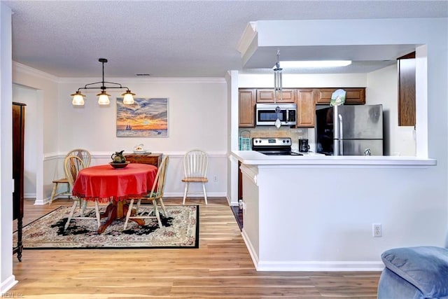 kitchen with stainless steel appliances, crown molding, pendant lighting, a textured ceiling, and light hardwood / wood-style floors