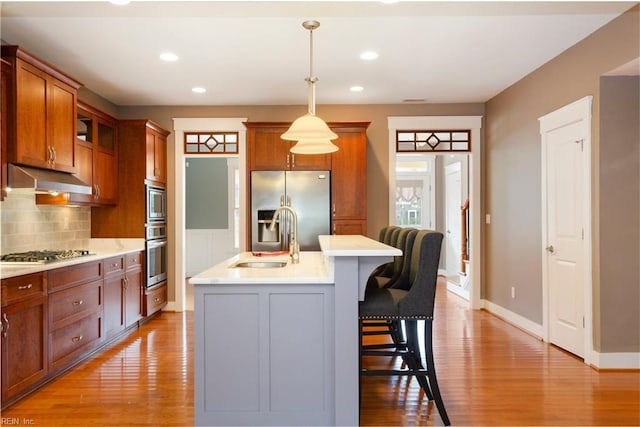 kitchen with appliances with stainless steel finishes, a breakfast bar, a kitchen island with sink, light hardwood / wood-style flooring, and hanging light fixtures