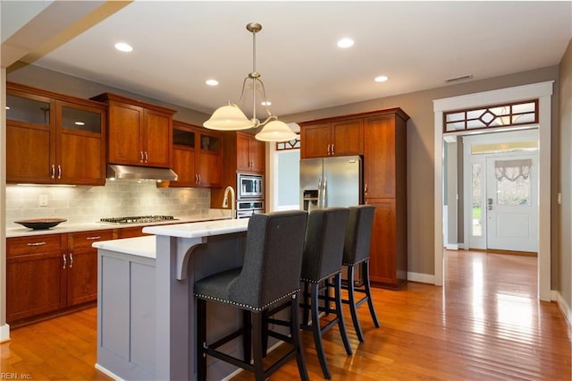 kitchen featuring appliances with stainless steel finishes, light wood-type flooring, a center island with sink, and pendant lighting