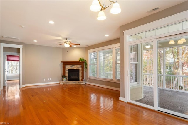 unfurnished living room with a fireplace, wood-type flooring, and ceiling fan with notable chandelier