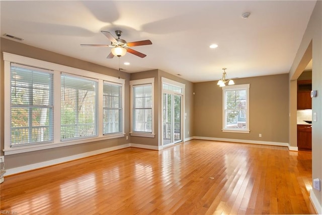 unfurnished living room with ceiling fan with notable chandelier and light hardwood / wood-style floors