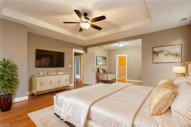 bedroom featuring hardwood / wood-style floors, ceiling fan, a raised ceiling, and ensuite bathroom