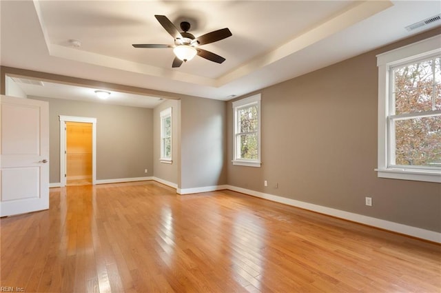 spare room featuring a raised ceiling, ceiling fan, and light hardwood / wood-style flooring