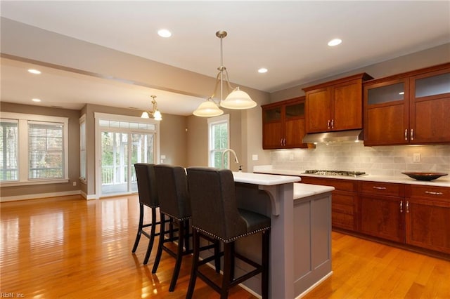 kitchen with tasteful backsplash, a breakfast bar, a kitchen island with sink, decorative light fixtures, and light hardwood / wood-style floors