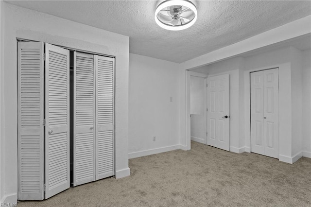 unfurnished bedroom featuring light colored carpet, a textured ceiling, and multiple closets