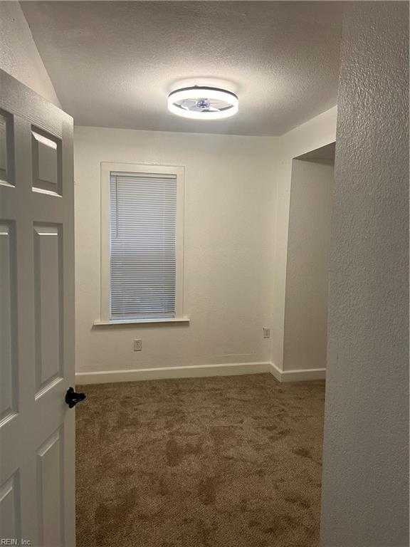 spare room featuring dark colored carpet and a textured ceiling