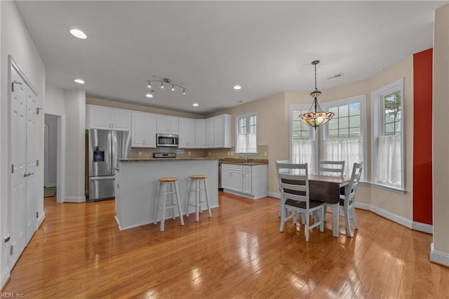 kitchen featuring pendant lighting, light hardwood / wood-style floors, appliances with stainless steel finishes, a kitchen island, and white cabinetry