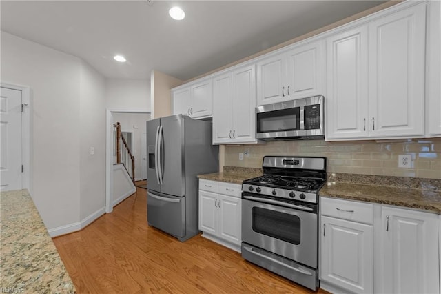 kitchen featuring light hardwood / wood-style flooring, dark stone counters, decorative backsplash, white cabinets, and appliances with stainless steel finishes