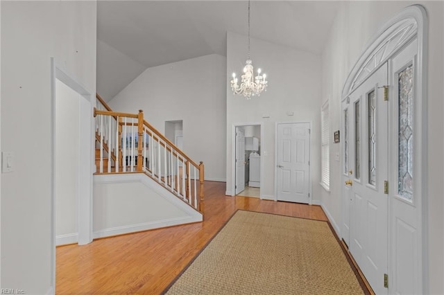 entrance foyer with hardwood / wood-style floors, washer / dryer, high vaulted ceiling, and an inviting chandelier