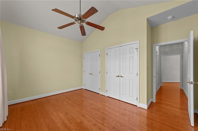 unfurnished bedroom with hardwood / wood-style flooring, ceiling fan, high vaulted ceiling, and two closets