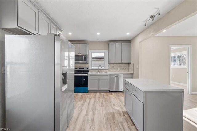 kitchen featuring decorative backsplash, light wood-type flooring, gray cabinetry, stainless steel appliances, and sink