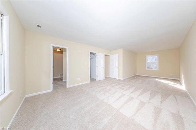 unfurnished bedroom with a closet, light colored carpet, ensuite bath, and a spacious closet