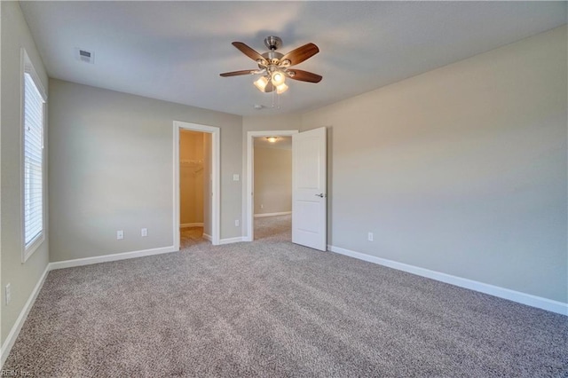 unfurnished bedroom with a walk in closet, ceiling fan, a closet, and carpet