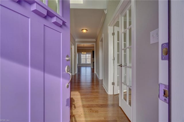 hallway featuring an inviting chandelier, light wood-type flooring, ornamental molding, and french doors