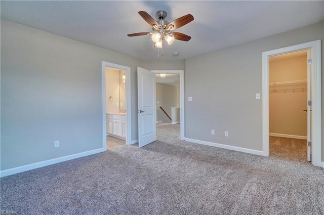 unfurnished bedroom with light carpet, ensuite bath, ceiling fan, a spacious closet, and a closet