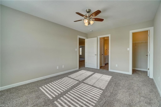 unfurnished bedroom featuring ceiling fan, ensuite bathroom, a walk in closet, a closet, and carpet