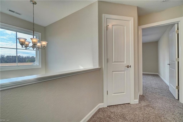 hallway with light carpet and an inviting chandelier