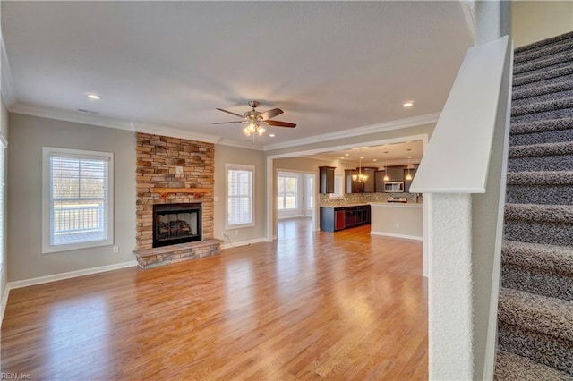 unfurnished living room with wood-type flooring, a stone fireplace, ceiling fan, and crown molding