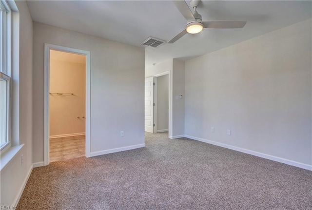 unfurnished bedroom with ceiling fan, a closet, a spacious closet, and light carpet