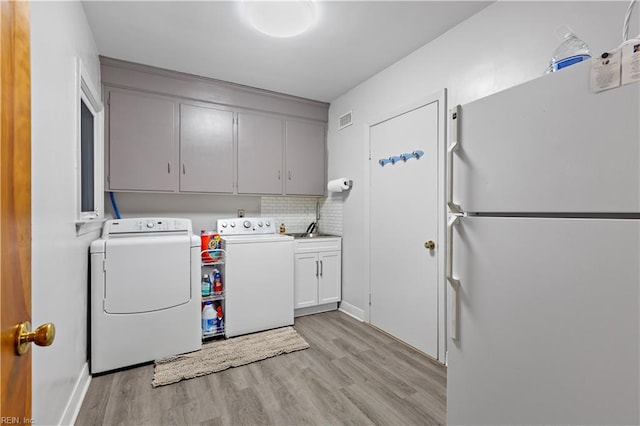 clothes washing area featuring cabinets, independent washer and dryer, sink, and light hardwood / wood-style flooring