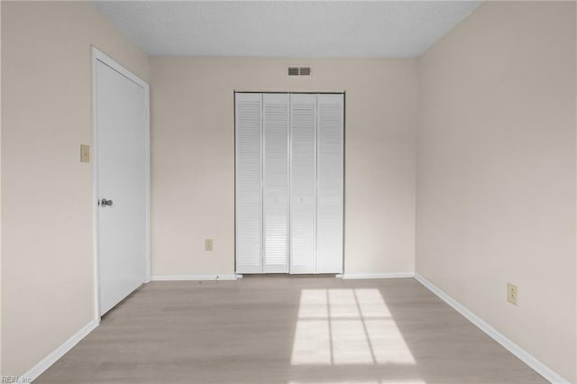 unfurnished bedroom featuring a closet, a textured ceiling, and light wood-type flooring