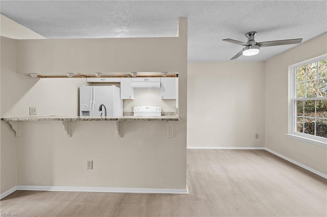 kitchen with light hardwood / wood-style flooring, a textured ceiling, white appliances, a kitchen bar, and white cabinets