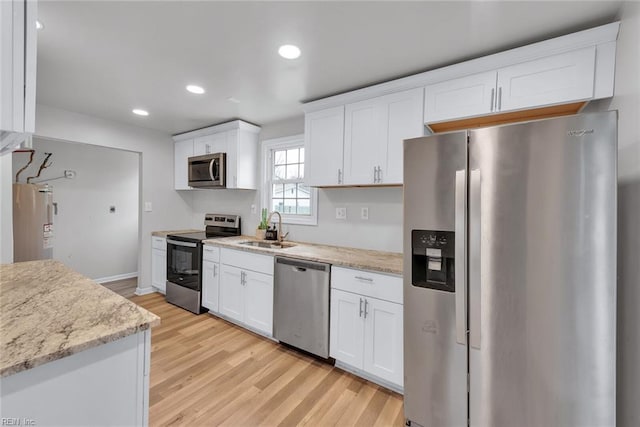 kitchen featuring light stone countertops, white cabinetry, sink, stainless steel appliances, and light hardwood / wood-style flooring