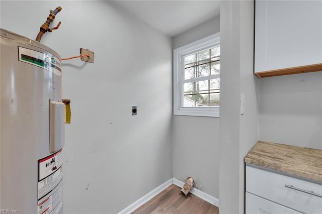 clothes washing area with electric dryer hookup, light hardwood / wood-style floors, cabinets, and electric water heater