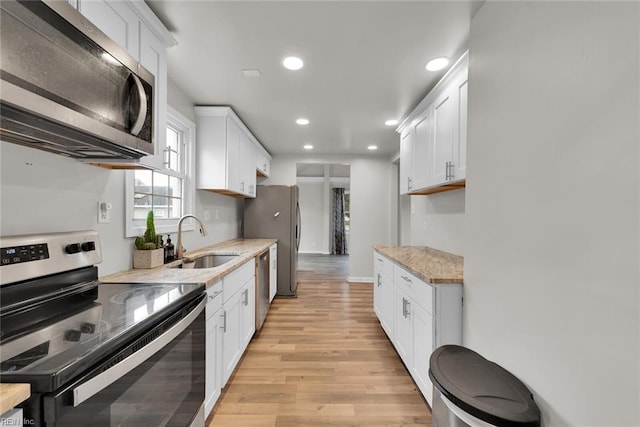 kitchen with sink, light stone countertops, light wood-type flooring, appliances with stainless steel finishes, and white cabinetry