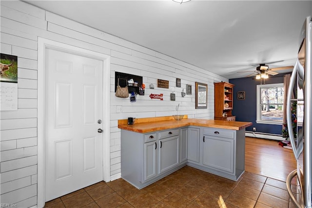 kitchen with dark tile patterned floors, butcher block countertops, ceiling fan, and a baseboard heating unit