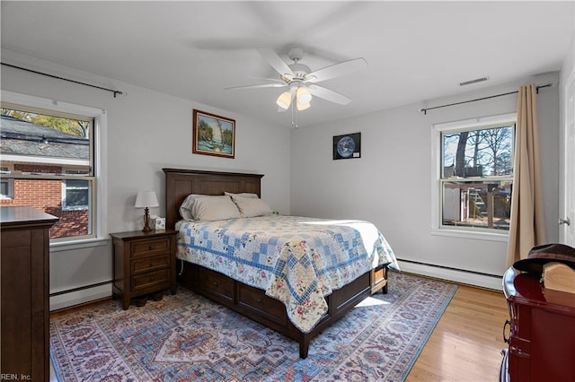 bedroom with ceiling fan, multiple windows, and a baseboard heating unit