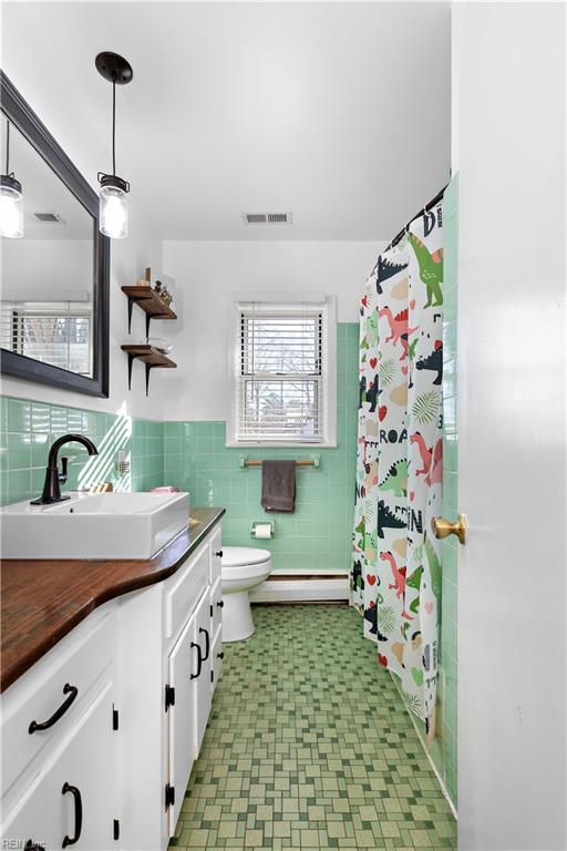 bathroom featuring vanity, toilet, tile walls, and a baseboard heating unit