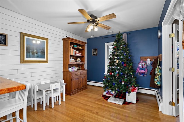 game room with light hardwood / wood-style floors, baseboard heating, ceiling fan, and wood walls