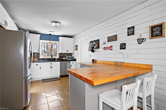 kitchen with white cabinetry, stainless steel appliances, butcher block countertops, pendant lighting, and a breakfast bar