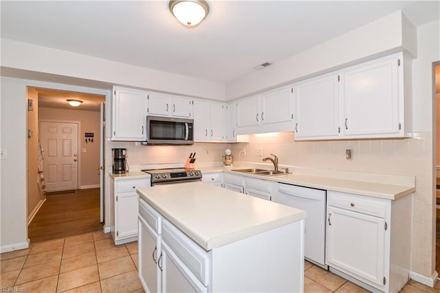 kitchen with sink, a center island, decorative backsplash, white cabinets, and appliances with stainless steel finishes