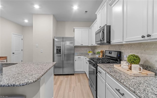 kitchen with appliances with stainless steel finishes, backsplash, light stone counters, light hardwood / wood-style floors, and white cabinetry