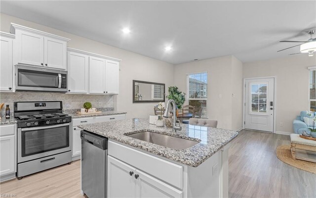 kitchen with appliances with stainless steel finishes, light wood-type flooring, sink, white cabinets, and an island with sink