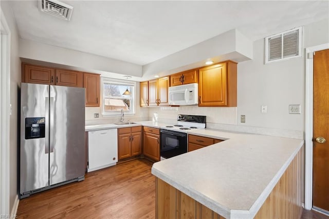 kitchen featuring kitchen peninsula, light wood-type flooring, white appliances, and sink