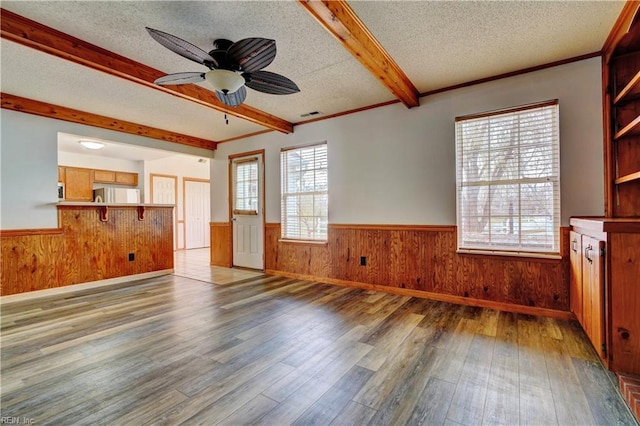 unfurnished living room with hardwood / wood-style floors, ceiling fan, a textured ceiling, and beamed ceiling