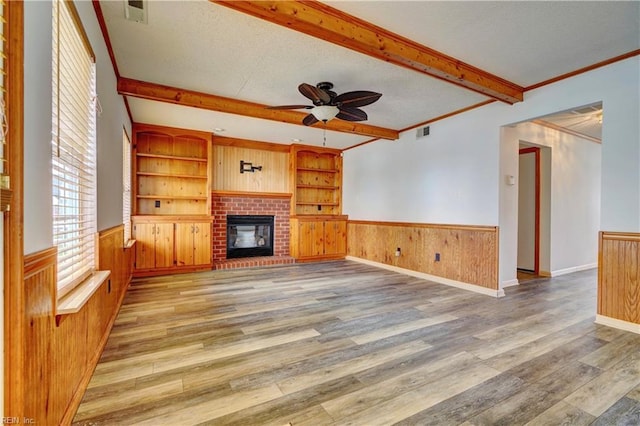 unfurnished living room featuring a brick fireplace, ceiling fan, beamed ceiling, and hardwood / wood-style flooring