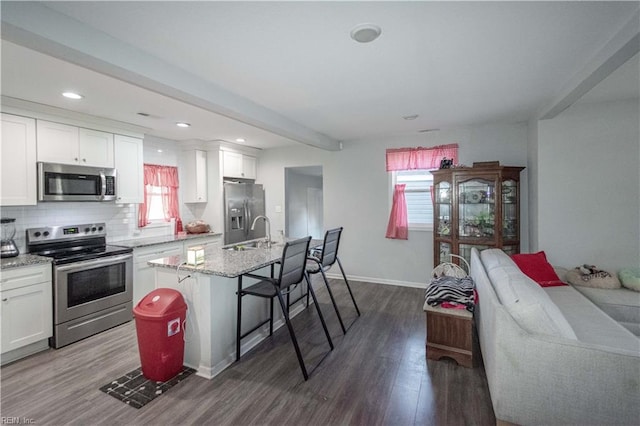 kitchen with stainless steel appliances, dark hardwood / wood-style flooring, an island with sink, a breakfast bar, and white cabinets